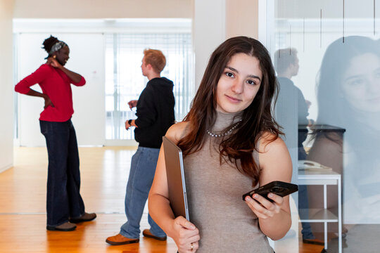 Female student holding smartphone and laptop at college