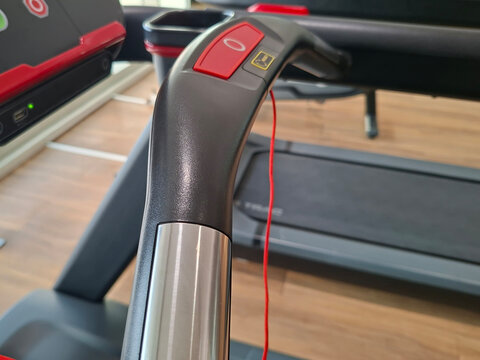 close-up shot of the curved black and silver handlebar of a fitness treadmill, featuring a red emergency stop or function button