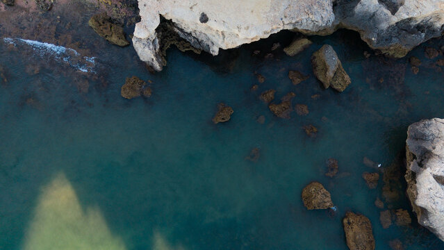 serene rock formations in clear coastal waters with waves crashing against the rocky shore from an aerial perspective, showcasing natural beauty and environmental conservation.