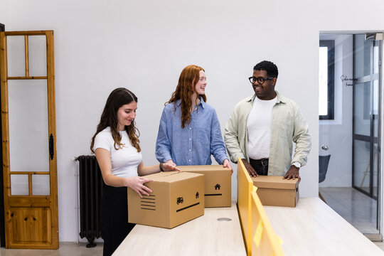Young coworkers packing cardboard boxes in modern office