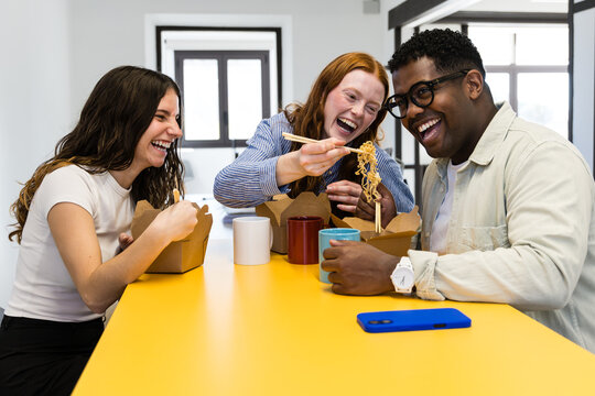 Coworkers enjoying lunch break with takeaway noodles at office