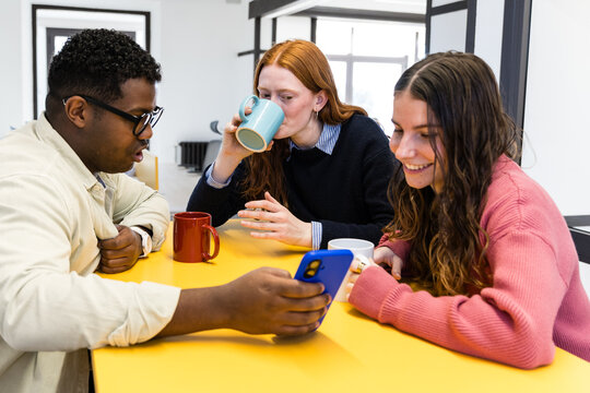 Colleagues sharing smartphone and coffee during office break