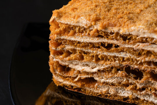Close-up of layered honey cake slice on dark plate
