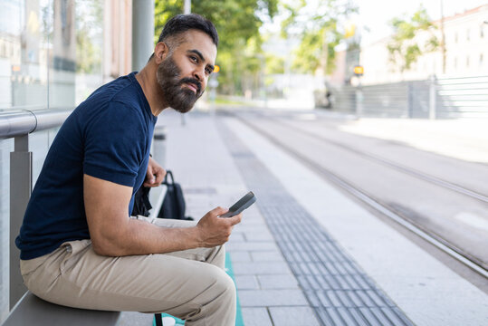 Indian man waiting at tram stop using smartphone outdoors