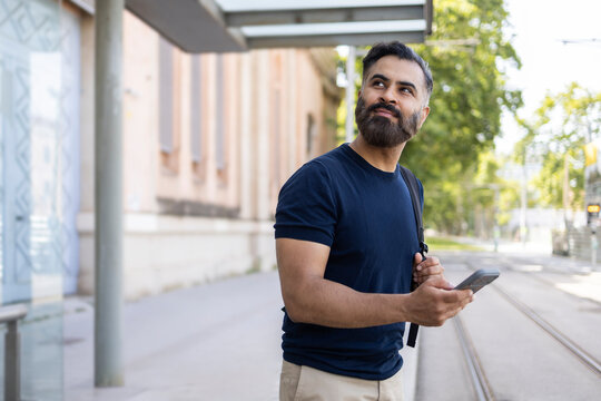 Indian man waiting at tram stop using smartphone outdoors