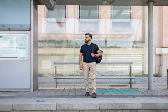 Indian man waiting at modern train stop with travel bag