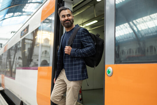 Indian commuter stepping off modern train with backpack