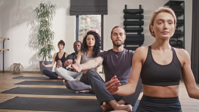 Meditating people sitting in row. Men and women clossing eyes and practicing meditation pose. Group of people doing padmasana at yoga studio. People sitting in lotuse pose at yoga session.