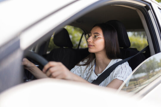 Young woman driving car wearing glasses and seat belt