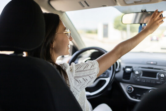 Woman driver adjusting rear view mirror in car interior