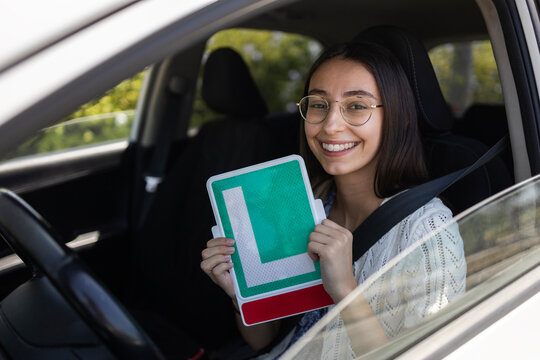 Smiling learner driver holding L plate sign in car seat