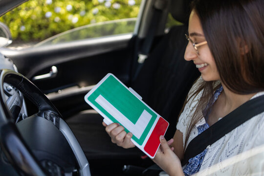 Young driver holding learner L-plate inside a car seat