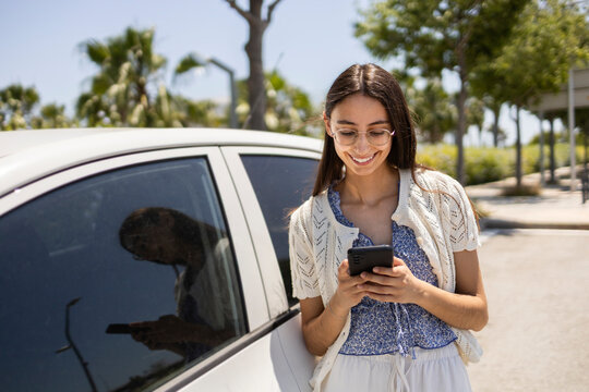 Young woman using smartphone beside parked car on street