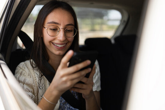 Smiling passenger using smartphone in back seat of car