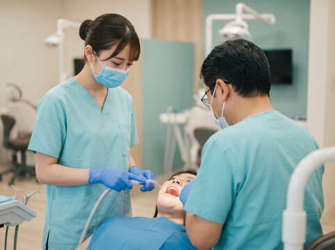ミントグリーンの制服で歯科医師の治療介助にあたる歯科助手