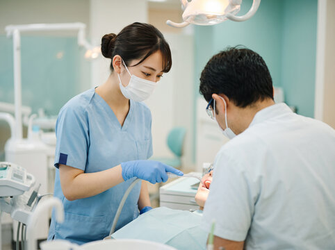 歯科治療で患者の口腔内バキュームを操作する歯科助手女性