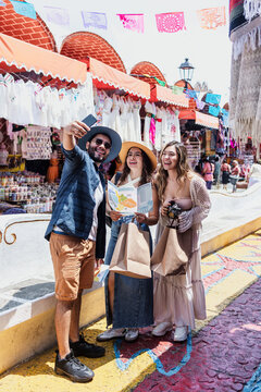 young latinos friends travellers taking a photo selfie in tourist market in Mexico Latin America, hispanic backpackers people in vacations
