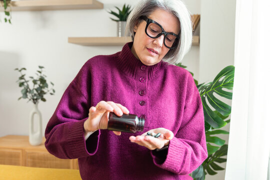 Senior woman taking vitamin supplement during home routine