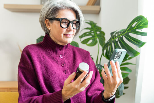 Senior woman checking vitamin bottle and smartphone at home