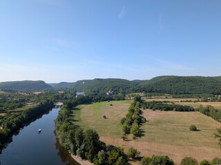Obraz premium High-angle panoramic view of the Dordogne River winding through a lush green valley with distant hills in Beynac-et-Cazenac, France