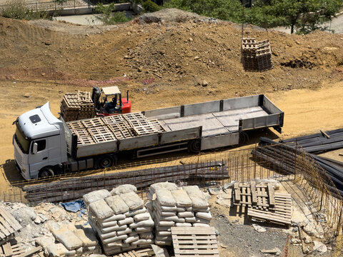 Forklift loading wooden pallet onto flatbed truck at site