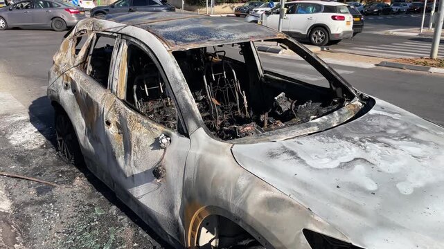 Burned passenger car with completely destroyed interior, shattered windows and severe fire damage parked on a city street after a vehicle fire