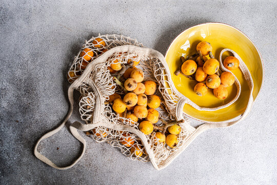 Fresh loquat fruit in reusable bag on gray background