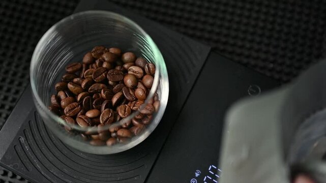 Slow motion footage while roasted coffee beans adding into a glass cup for measuring weight.