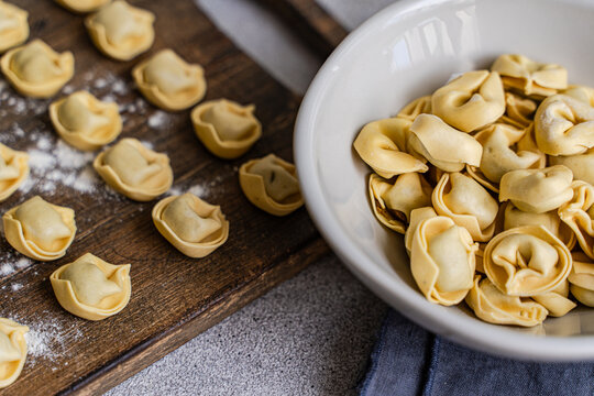 Homemade tortellini on wooden board with flour and bowl