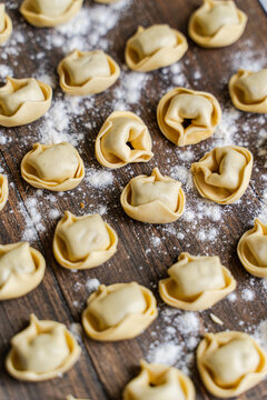 Homemade tortellini on floured wooden board, closeup