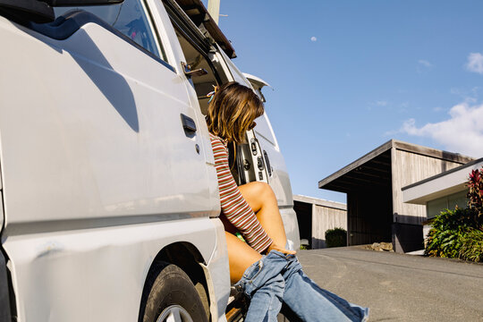 Young surfer changing in van doorway on sunny coastal street
