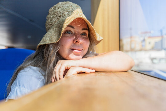 Young woman in straw hat gazing from train window in summer