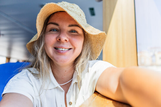 Smiling woman in sun hat taking selfie on ferry deck