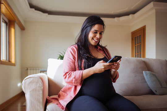 Pregnant woman using smartphone on sofa at home
