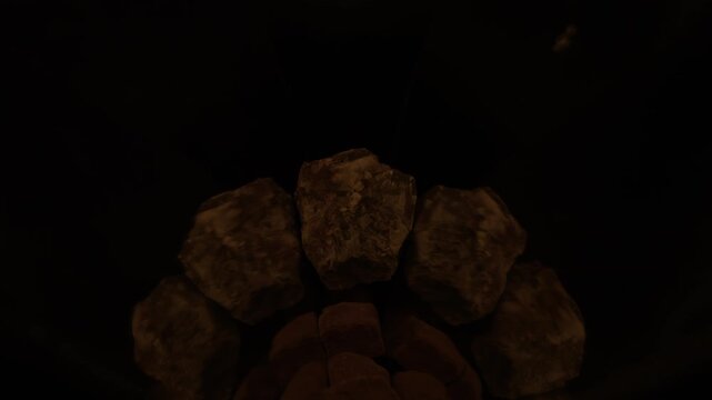 A dense fire cap creates a bright luminous contrast against a dark granite stone in 1000fps slow motion. Perfectly mirrored symmetry in absolute darkness with no sunset background. Concept: contrast