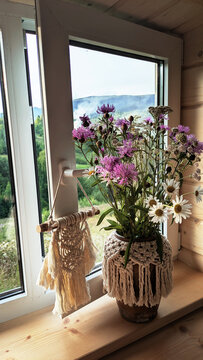 A vase with a bouquet of wildflowers and daisies on a windowsill