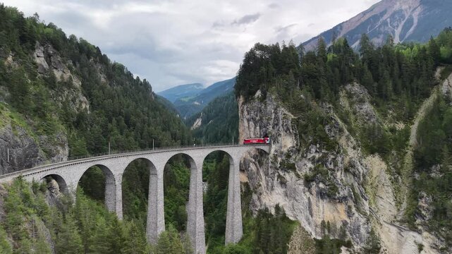 Cinematic aerial drone footage of the iconic panoramic train crossing the Landwasser Viaduct, showcasing the breathtaking alpine landscape of the Swiss Alps in Graub&uuml;nden &ndash; 2026
