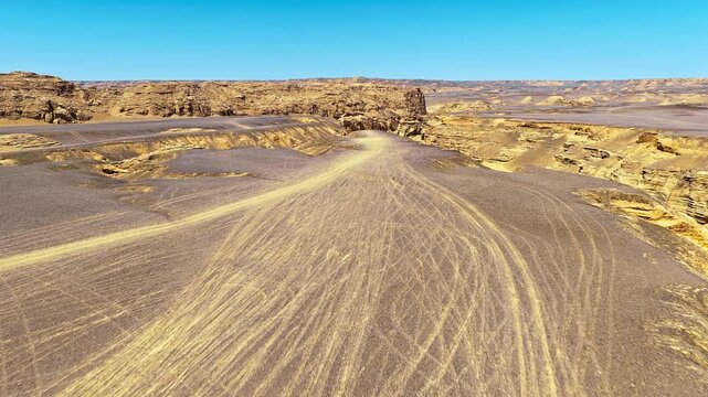 Aerial view of rugged desert canyons with tire tracks on the plateau in Xinjiang, China.