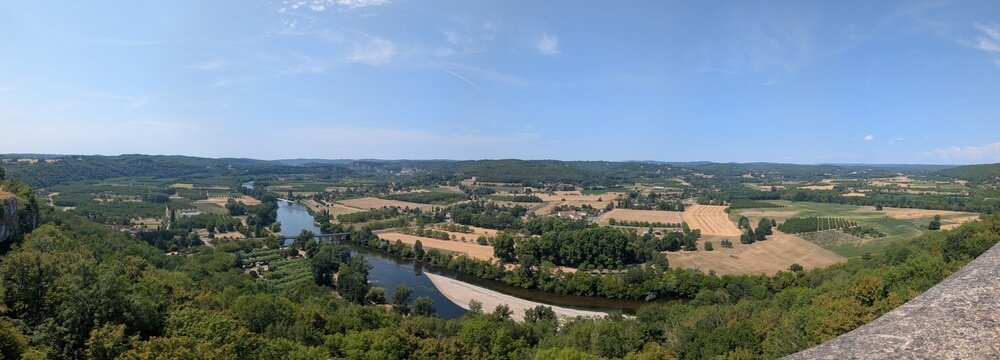 Wide panoramic high-angle viewpoint overlooking the expansive Dordogne River valley, checkerboard fields, and distant hills from the bastide town of Domme, France