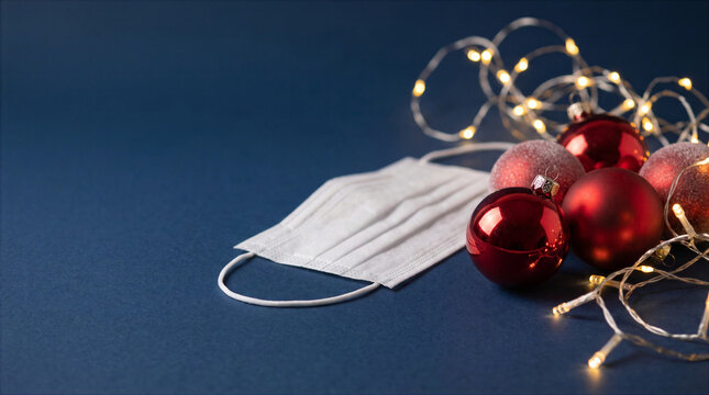 Medical face mask with red Christmas baubles and fairy lights on dark blue background
