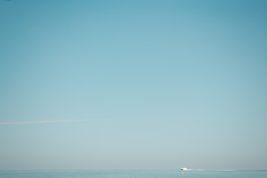 A distant boat moves across calm blue water beneath a wide, cloudless sky with extensive copy space. This image highlights peaceful travel, open water, minimal scenery, and summer recreation