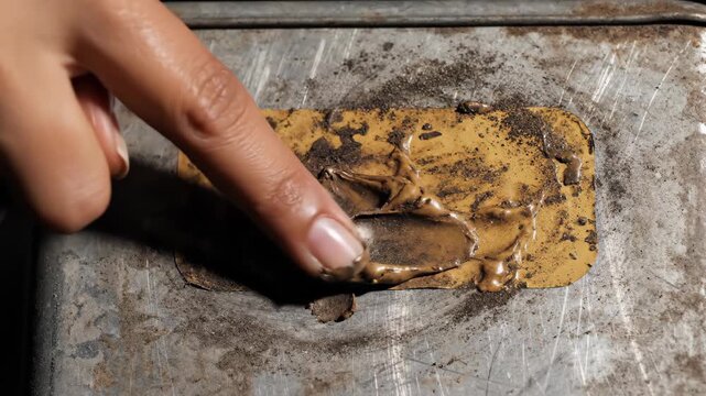 Close-up of hands pressing nuts and creamy spread onto a rectangular food item.