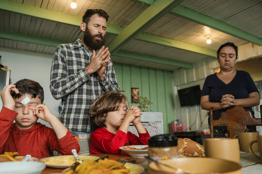 Family members praying before sharing a meal at home