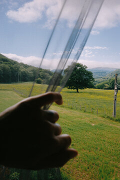 Hand holding sheer fabric by the window with a green landscape