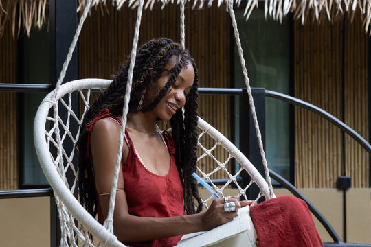 smiling Woman Journaling in Hanging Chair, write in notebook