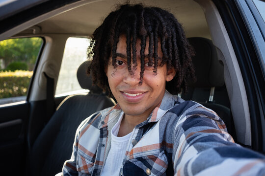 A young man smiling as he takes a selfie with his phone inside the car