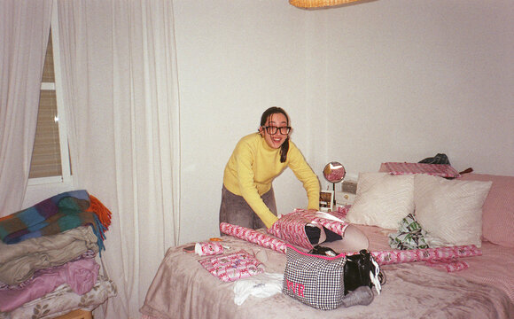 Smiling young woman wrapping gifts on a bed at home