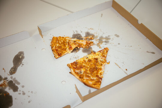 Leftover pizza slices with grease stains in empty cardboard box