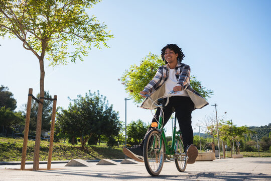 A smiling young man riding a bike in a park on a sunny day. Copy space