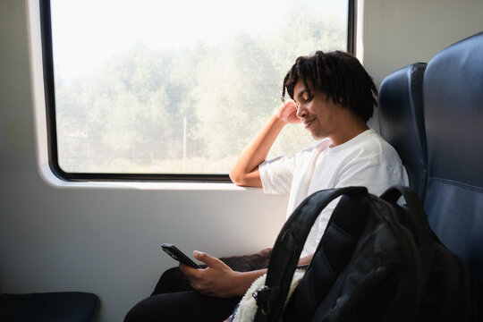 Young Man on Train Looks at Phone During Trip. Copy space